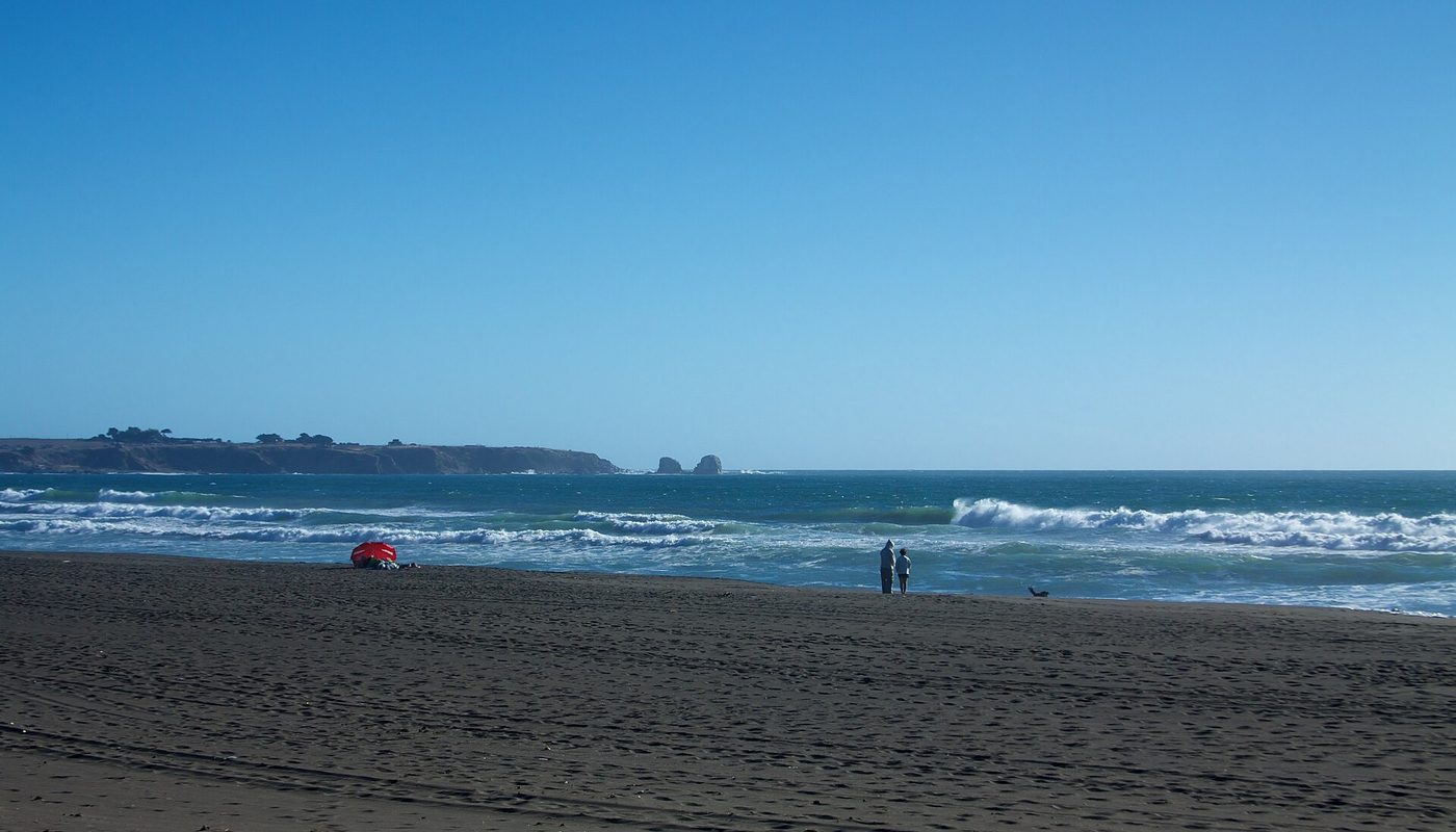 Playa Hermosa de Pichilemu en un día despejado, con la arena oscura y el mar al fondo