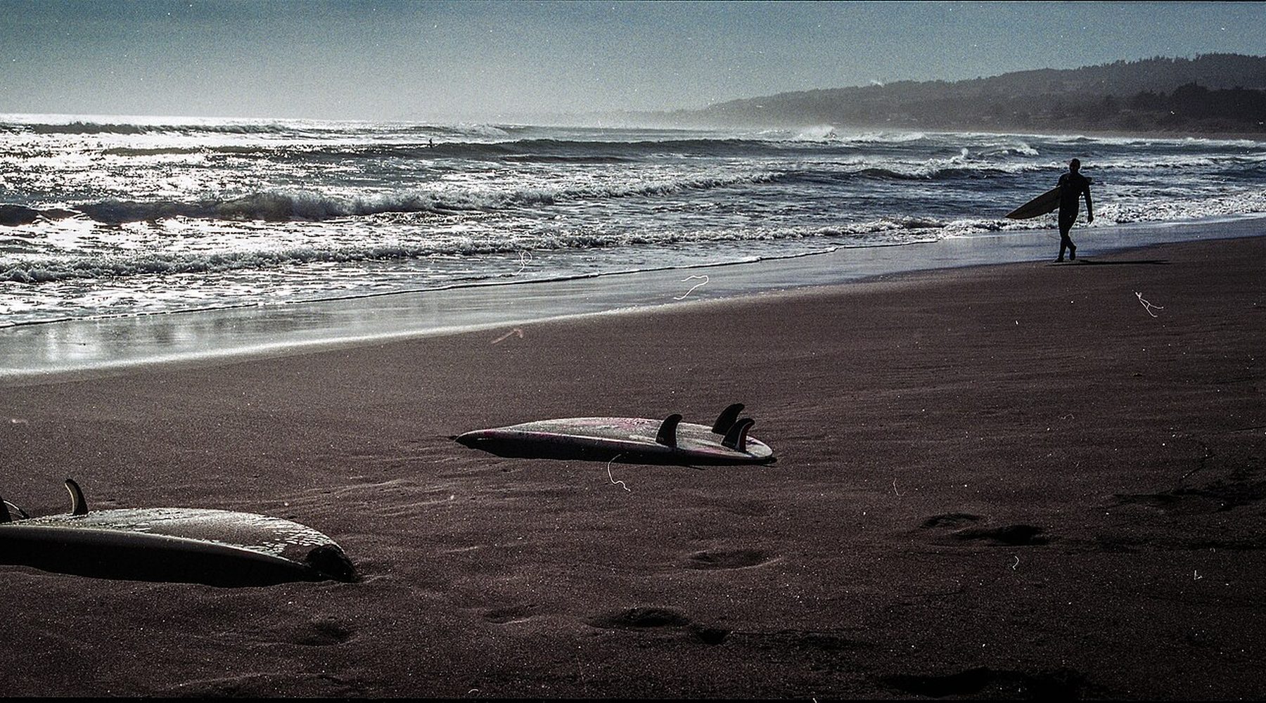 Atardecer en la playa de Punta de Lobos, con dos tablas de surf en la arena y un surfista caminando hacia el mar
